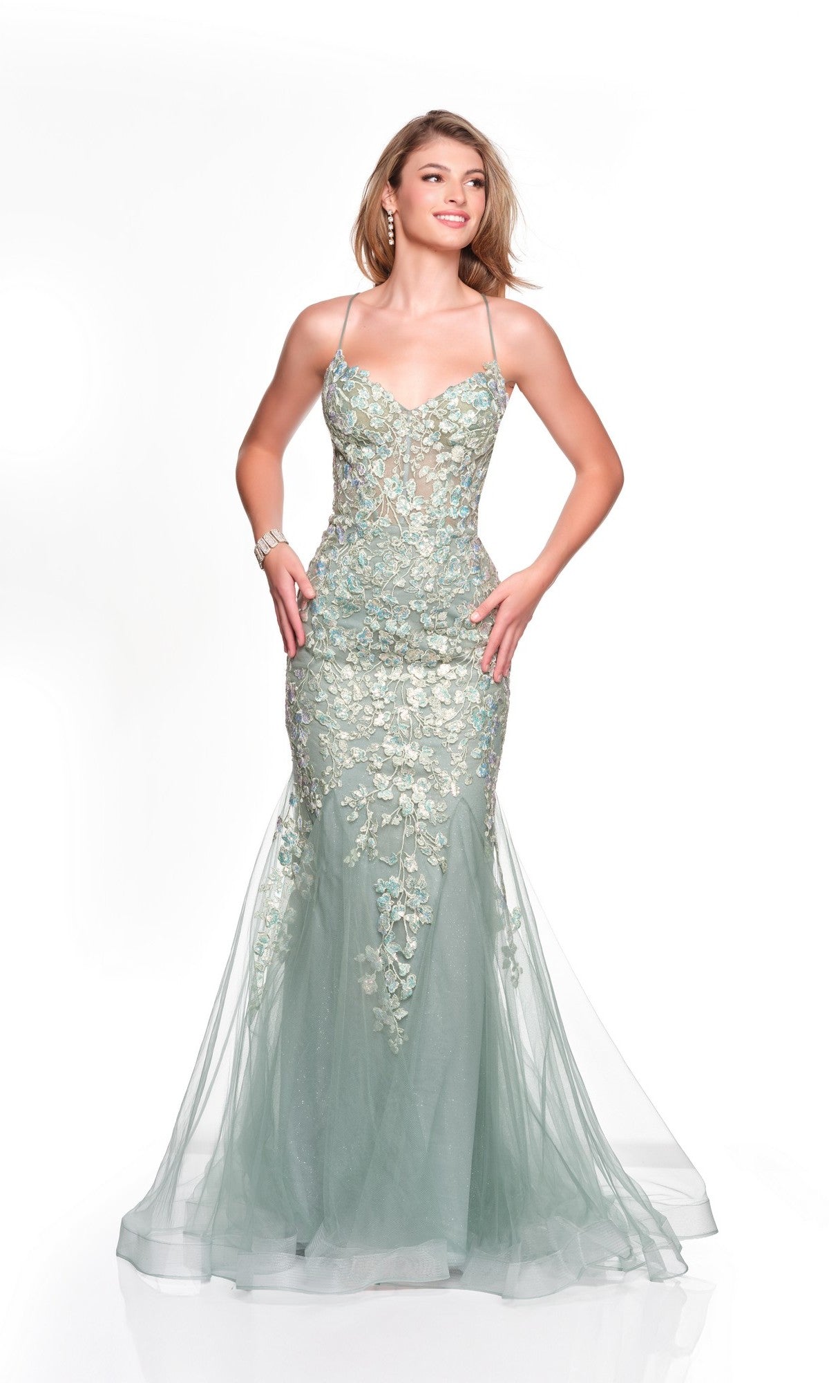 A woman poses with hands on hips in the Dave and Johnny 12924 long prom dress, a mermaid gown in light green with embroidery appliques, sheer accents, and a lace-up open back, set against a white background.